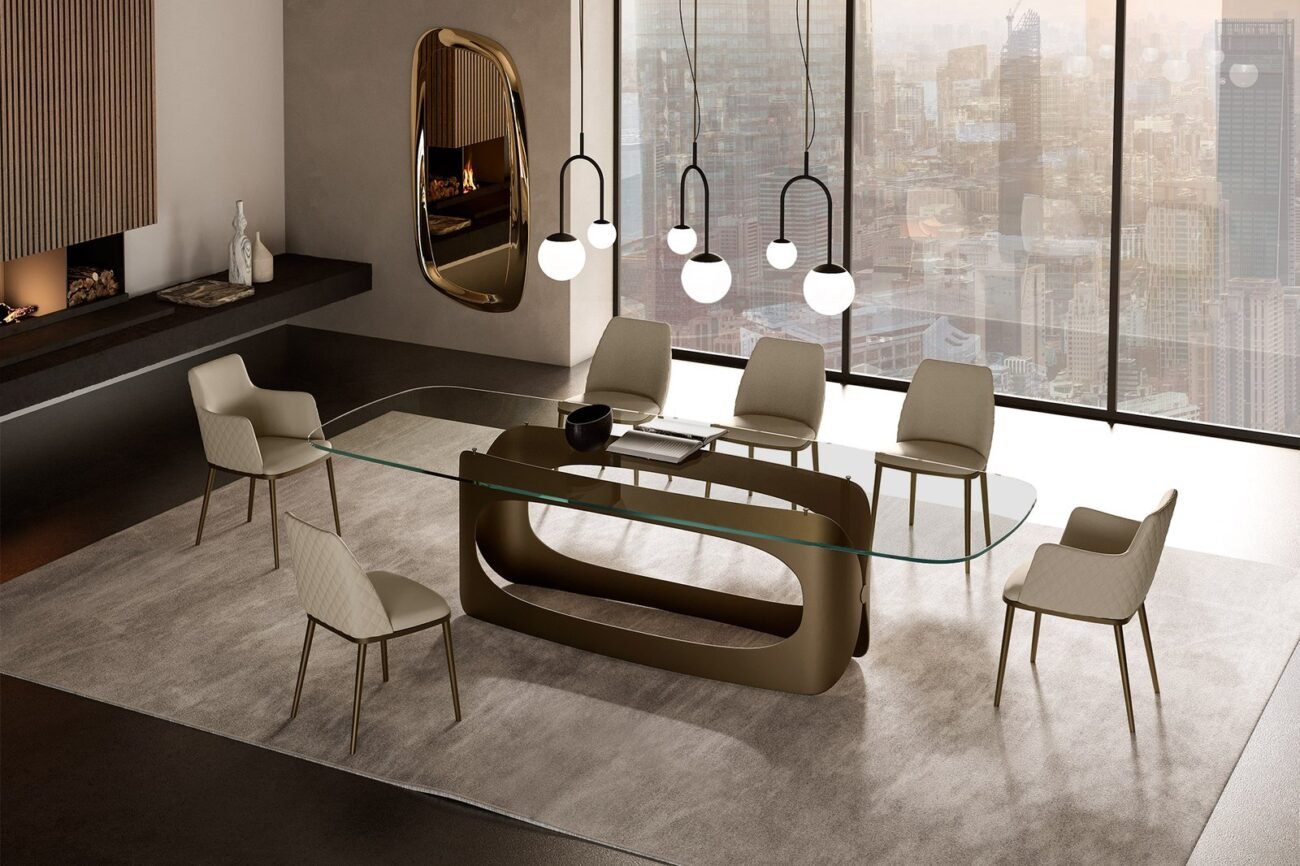 Une salle à manger contemporaine avec la table en verre métallique MAX DIAMOND, entourée de six chaises beiges. Un grand miroir orne le mur, tandis que des suspensions illuminent l'espace au-dessus de la table. Les fenêtres du sol au plafond offrent une vue imprenable sur l'horizon de la ville, complétée par un tapis neutre sous les pieds. Meubles Barret Bordeaux